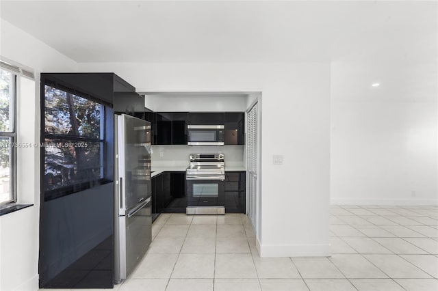 kitchen with light tile patterned floors, stainless steel appliances, baseboards, light countertops, and dark cabinetry