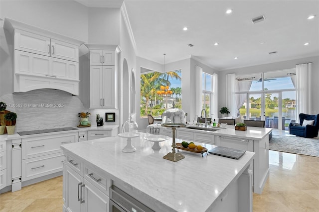 kitchen with sink, crown molding, backsplash, a kitchen island, and black electric cooktop