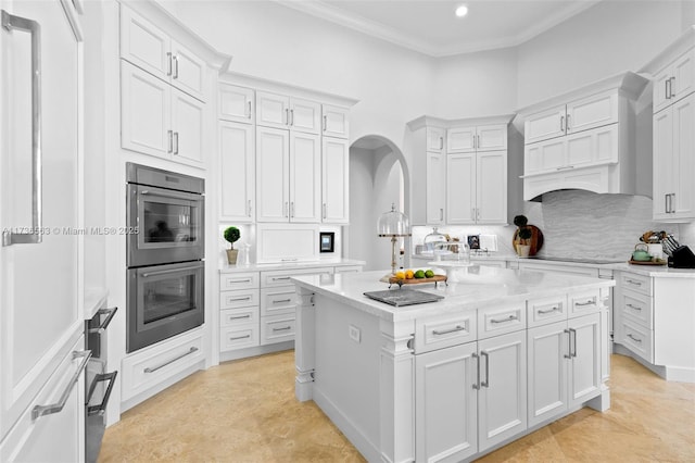 kitchen featuring crown molding, tasteful backsplash, double oven, a kitchen island, and white cabinets