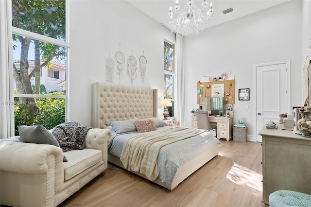 bedroom featuring an inviting chandelier, light hardwood / wood-style floors, and a high ceiling