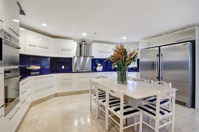 kitchen with wall chimney exhaust hood, tasteful backsplash, light tile patterned floors, stainless steel appliances, and white cabinets