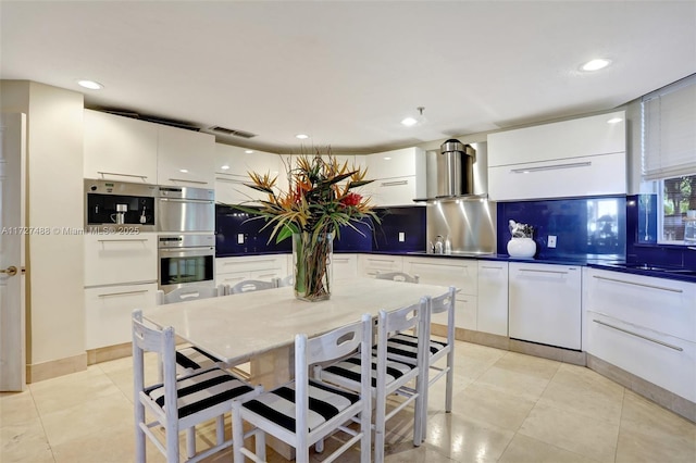 kitchen with visible vents, white dishwasher, wall chimney exhaust hood, and modern cabinets