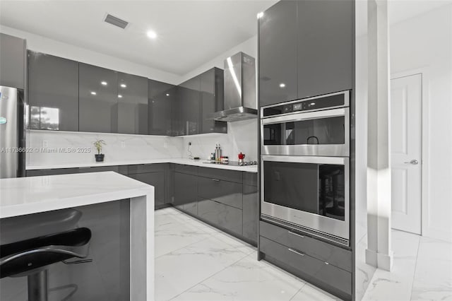 kitchen with tasteful backsplash, stainless steel appliances, gray cabinets, and wall chimney range hood