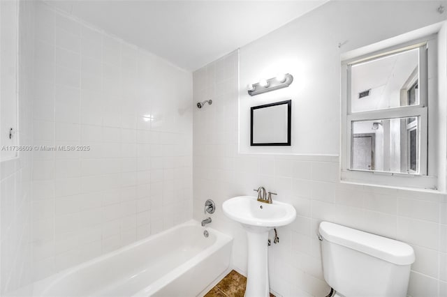 bathroom with tile walls, tiled shower / bath combo, tile patterned floors, and toilet