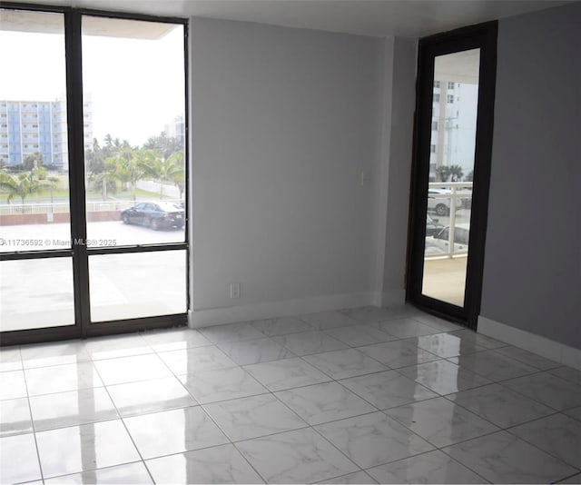 empty room with expansive windows, marble finish floor, a view of city, and baseboards