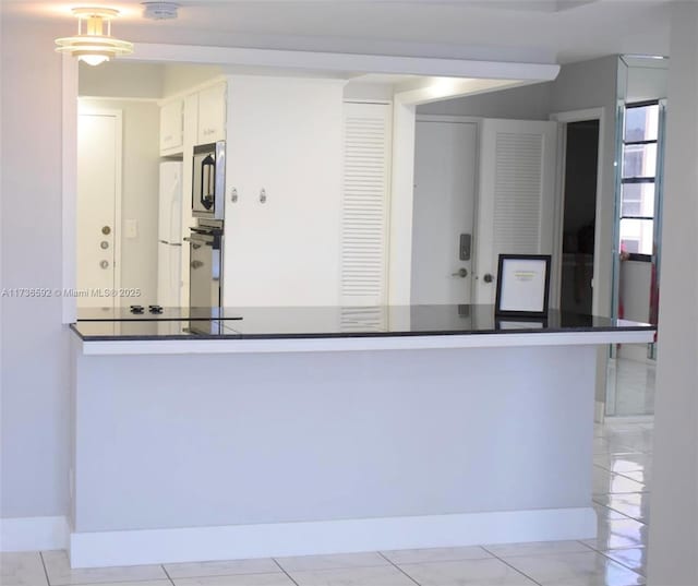 kitchen with marble finish floor, dark countertops, stainless steel microwave, freestanding refrigerator, and white cabinets