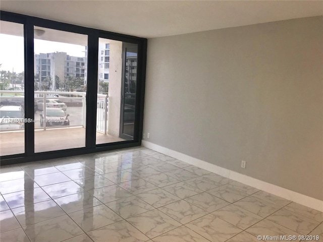 empty room featuring marble finish floor, a wall of windows, a city view, and baseboards