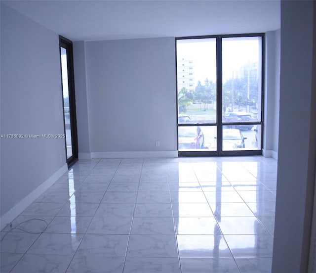 unfurnished room with marble finish floor, baseboards, and a wall of windows