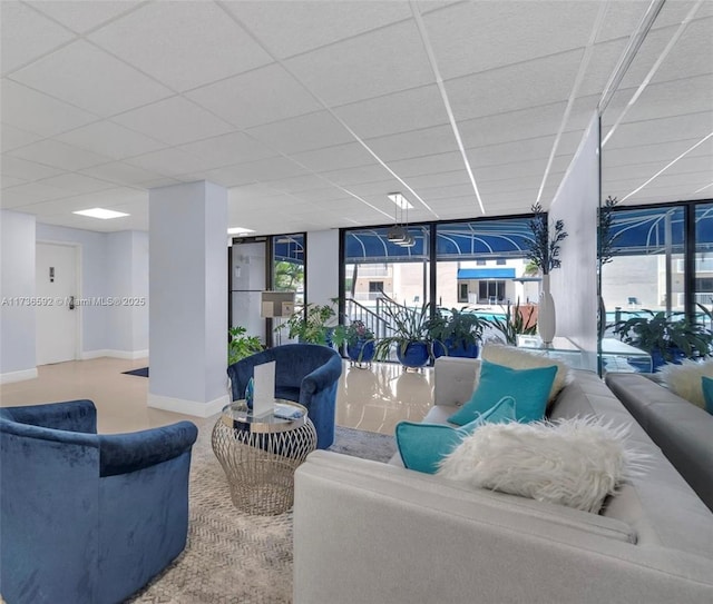 living room featuring a drop ceiling, a wall of windows, and baseboards