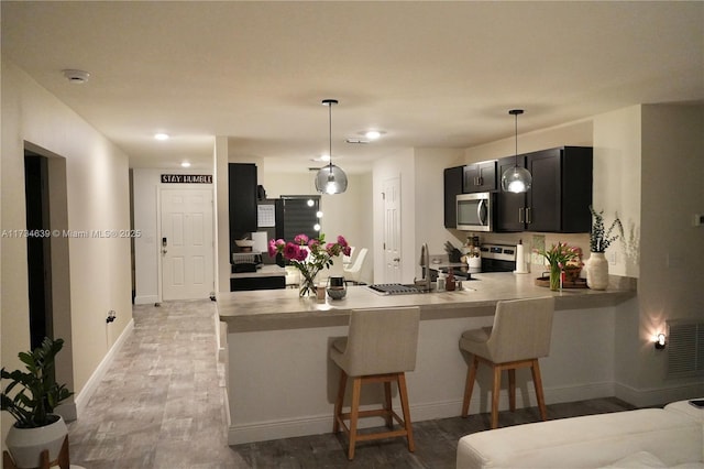 kitchen featuring stainless steel appliances, a peninsula, light wood-style floors, dark cabinets, and a breakfast bar