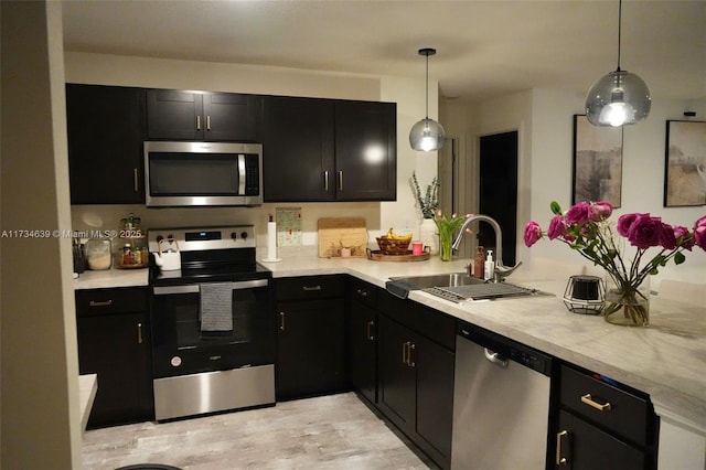 kitchen featuring decorative light fixtures, sink, kitchen peninsula, stainless steel appliances, and light hardwood / wood-style flooring