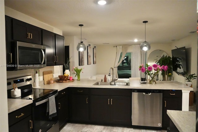 kitchen featuring a sink, dark cabinetry, stainless steel appliances, light countertops, and a peninsula