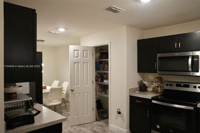 kitchen with stainless steel appliances, light countertops, baseboards, dark cabinets, and visible vents