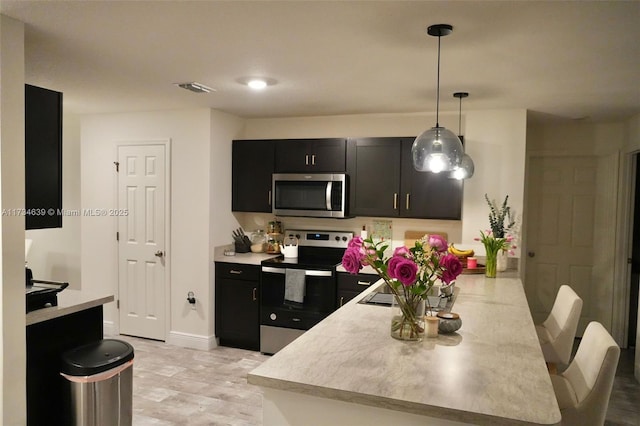 kitchen featuring a peninsula, stainless steel appliances, visible vents, and dark cabinetry
