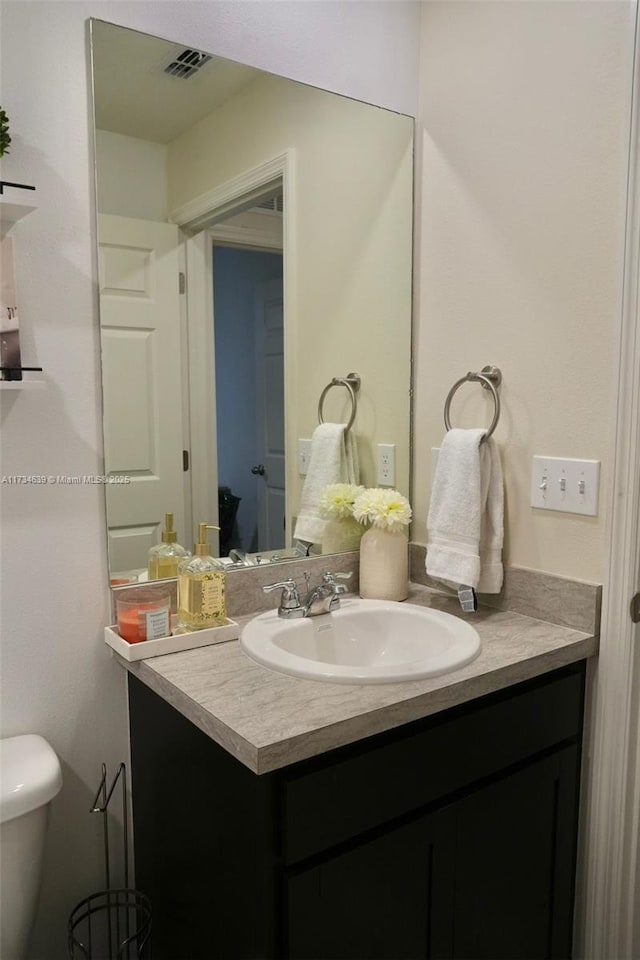 bathroom with toilet, vanity, and visible vents