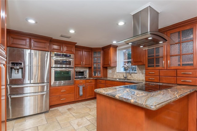 kitchen with sink, appliances with stainless steel finishes, dark stone countertops, island exhaust hood, and kitchen peninsula