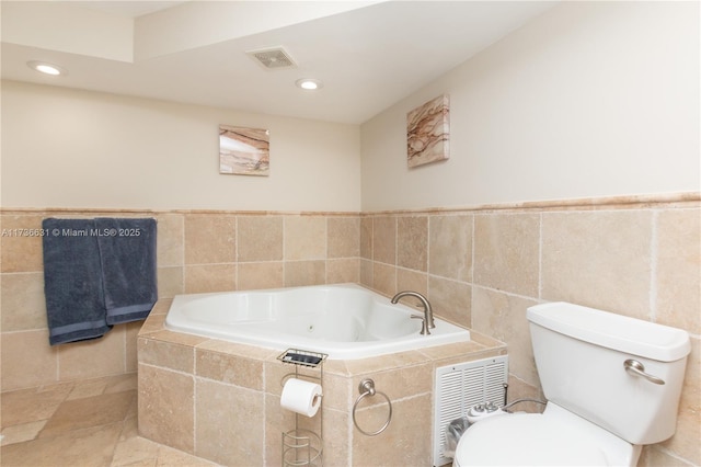 bathroom featuring tile walls, tiled tub, and toilet