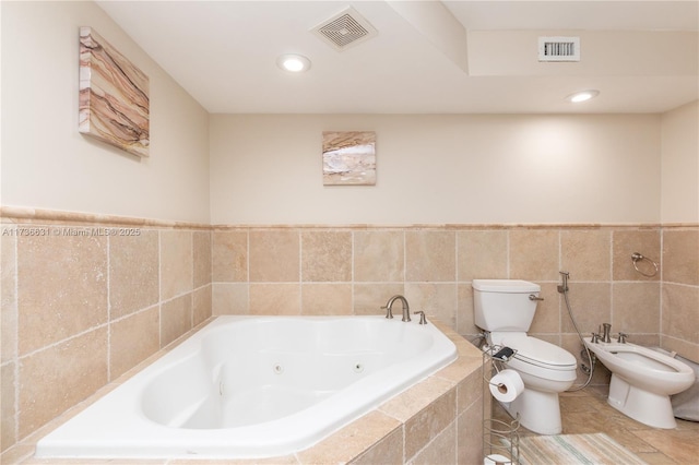 bathroom with a bidet, tiled tub, tile walls, and toilet