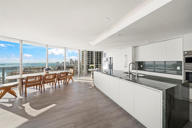 kitchen featuring sink, white cabinetry, a water view, hardwood / wood-style flooring, and a wall of windows