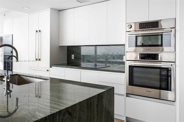 kitchen featuring sink, white cabinetry, dark stone countertops, tasteful backsplash, and stainless steel double oven