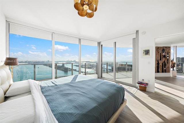 bedroom with a water view, expansive windows, hardwood / wood-style floors, and access to outside