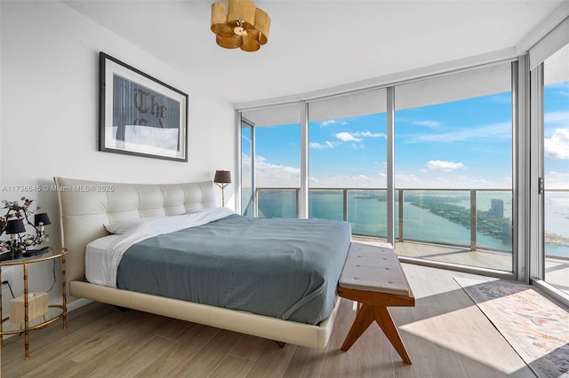 bedroom featuring multiple windows, a wall of windows, access to outside, a water view, and light hardwood / wood-style flooring