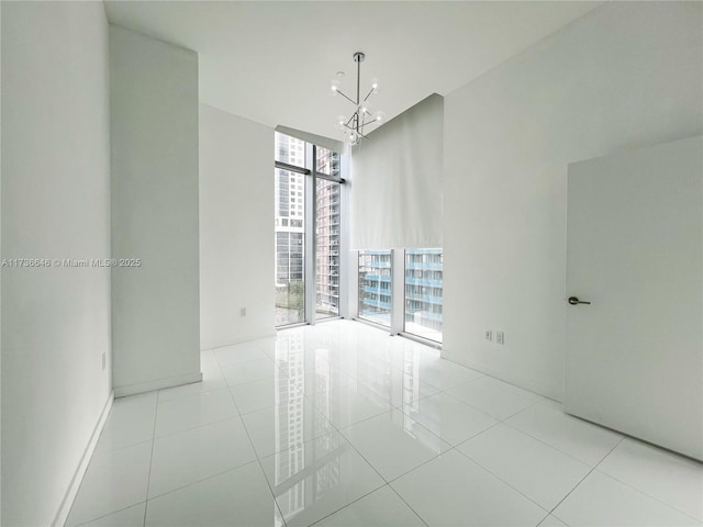 empty room with a notable chandelier, floor to ceiling windows, and light tile patterned floors