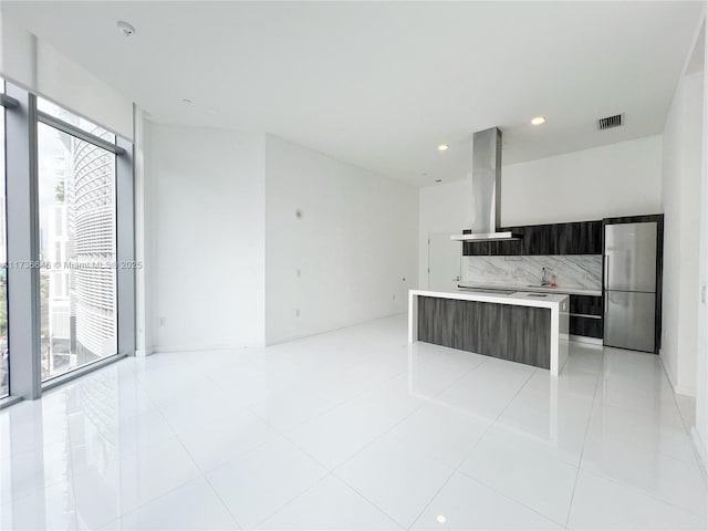 kitchen featuring a center island, light tile patterned floors, stainless steel refrigerator, island exhaust hood, and decorative backsplash