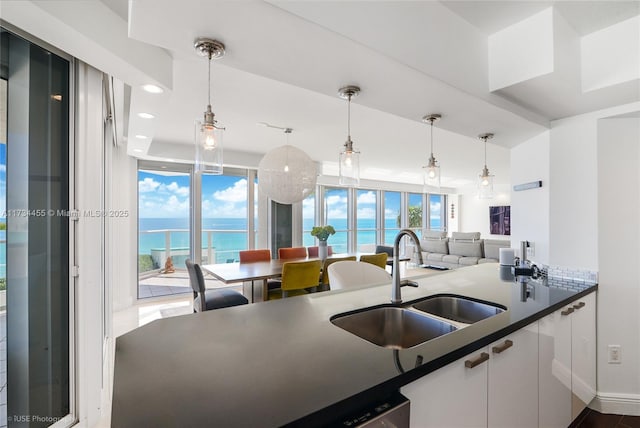 kitchen featuring sink, white cabinetry, a water view, a wealth of natural light, and decorative light fixtures