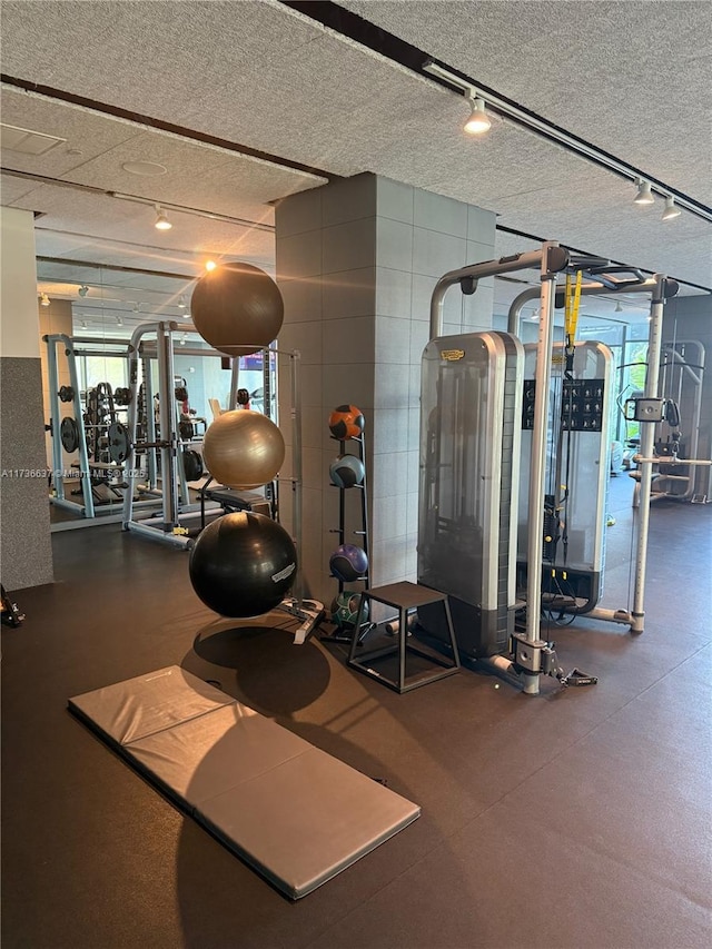 gym with rail lighting, plenty of natural light, and a textured ceiling