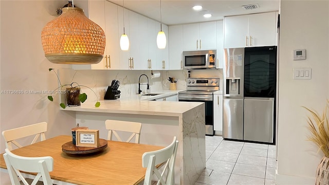 kitchen featuring appliances with stainless steel finishes, a sink, white cabinets, and pendant lighting