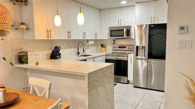 kitchen with appliances with stainless steel finishes, sink, white cabinets, light stone counters, and kitchen peninsula