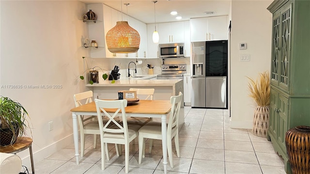 kitchen with appliances with stainless steel finishes, light countertops, white cabinetry, pendant lighting, and a sink