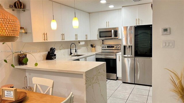 kitchen with light stone counters, a peninsula, a sink, white cabinetry, and appliances with stainless steel finishes