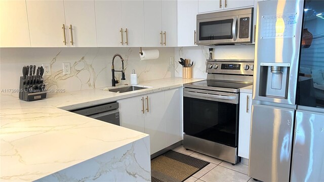 kitchen featuring stainless steel appliances, a sink, white cabinetry, and light stone countertops