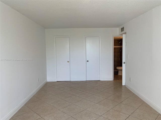 unfurnished bedroom featuring light tile patterned floors, ensuite bath, and a textured ceiling