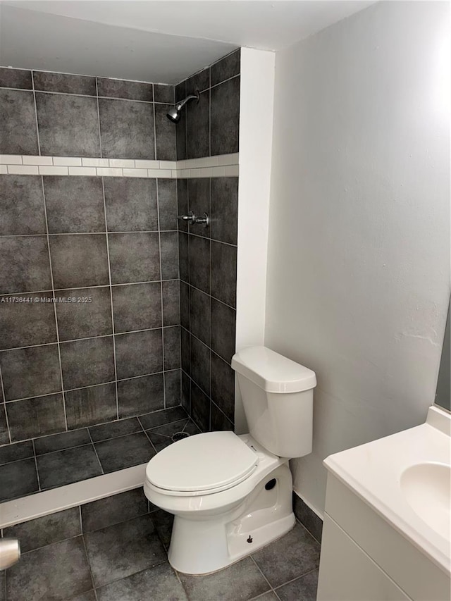 bathroom featuring vanity, a tile shower, tile patterned floors, and toilet