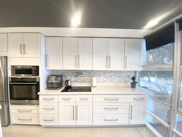 kitchen with tasteful backsplash, stainless steel fridge, white cabinets, light tile patterned floors, and black electric cooktop