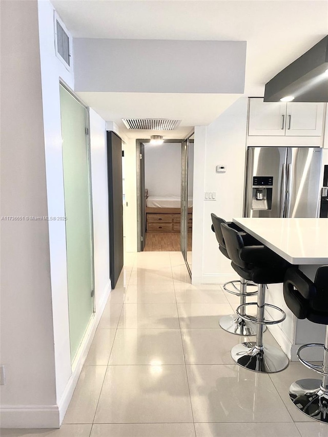 kitchen with white cabinetry, a breakfast bar, light tile patterned floors, and stainless steel fridge