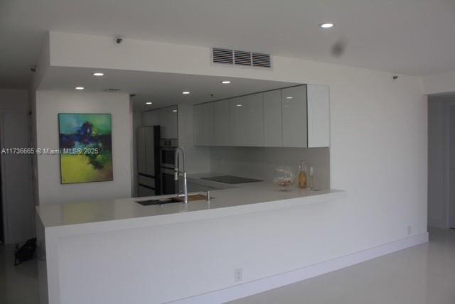 kitchen with a sink, light countertops, a peninsula, visible vents, and modern cabinets