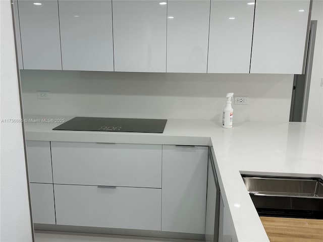 kitchen featuring light countertops, modern cabinets, black electric stovetop, and white cabinetry
