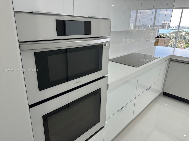 kitchen with modern cabinets, light countertops, white cabinets, double oven, and black electric stovetop