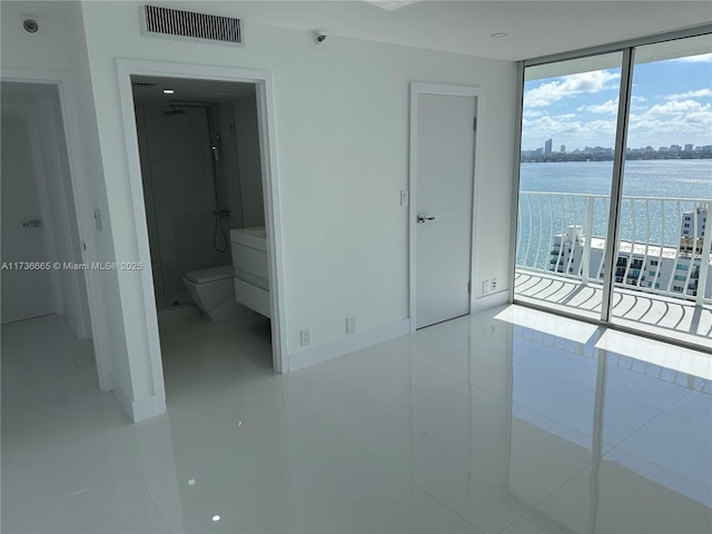 unfurnished bedroom featuring a wall of windows, access to exterior, visible vents, tile patterned floors, and a water view