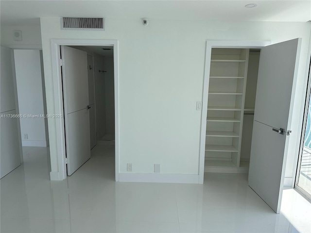 unfurnished bedroom featuring a spacious closet, light tile patterned floors, visible vents, and a closet
