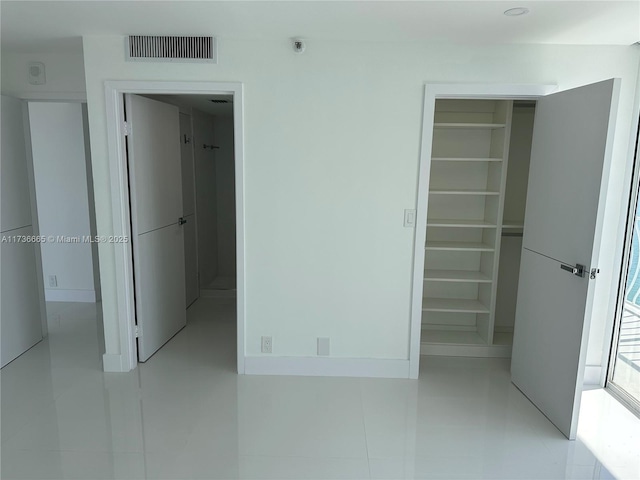 unfurnished bedroom with a closet, light tile patterned flooring, a walk in closet, and visible vents