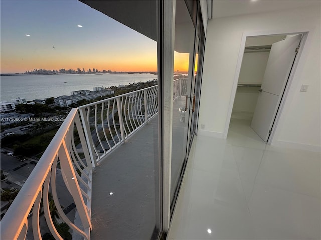 balcony at dusk featuring a water view