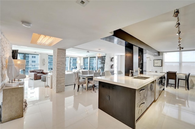 kitchen featuring decorative columns, rail lighting, sink, light tile patterned floors, and a center island with sink