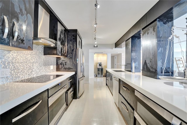 kitchen with wall chimney exhaust hood, rail lighting, light tile patterned floors, appliances with stainless steel finishes, and backsplash