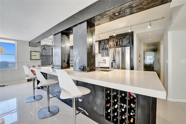 kitchen with light tile patterned flooring, rail lighting, sink, stainless steel fridge, and backsplash