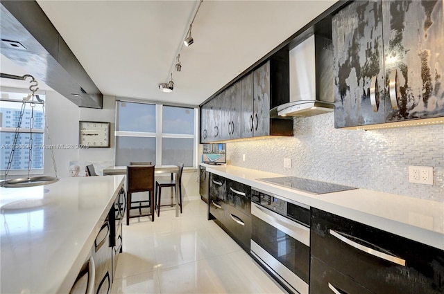 kitchen with track lighting, black electric stovetop, oven, decorative backsplash, and wall chimney range hood